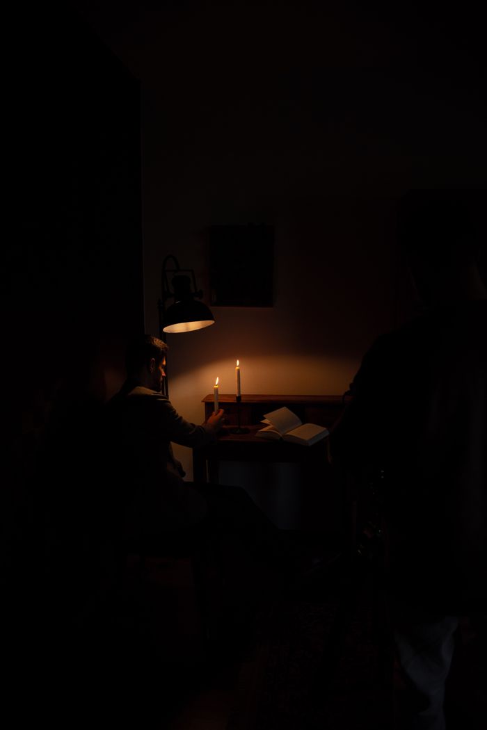 A man sits alone with a candle and book, creating an intimate, moody atmosphere.